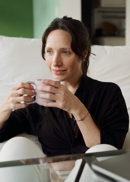 Woman Enjoying a Drink While Sitting on a Couch in a Cozy Room