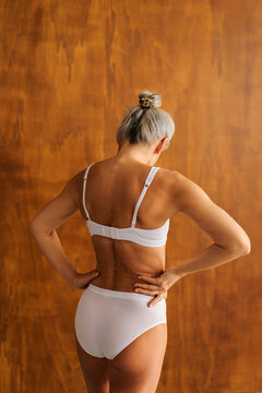 Mature woman standing in underwear, hands on lower back