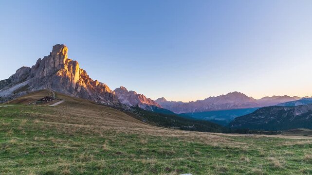 Time lapse of golden sunrise light on Ra Gusela peak at Passo Giau, Dolomites, Italy. Shadows creep across an alpine meadow under a clear sky. Serenity, passing time and freedom in the mountains