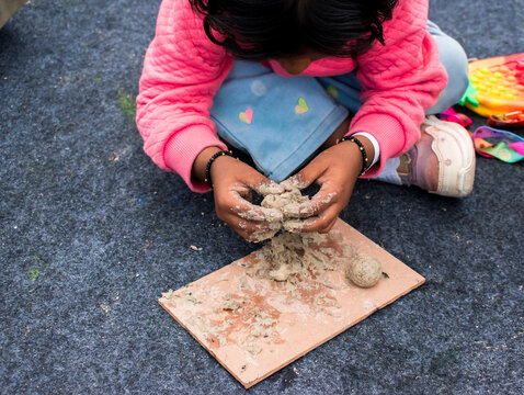 Little girl making a handmade clay craft while sitting on the floor, shaping wet clay with her hands