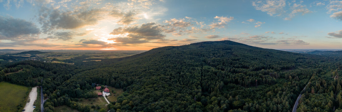 Aerial view of Sleza Mountain at sunset from Przelecz Tapadla in summer, surrounded by dense forests and rolling hills in Sleza Landscape Park, Lower Silesia, Poland.