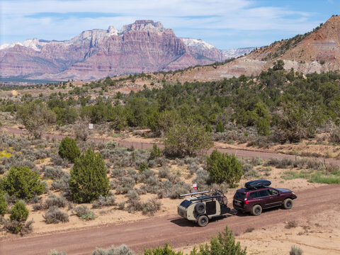Aerial view of an SUV pulling a teardrop camper trailer on a dirt road on Gooseberry Mesa with the red rock cliffs of Zion National Park in the background, Hurricane, Utah, United States.