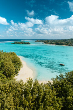 Aerial view of the turquoise lagoon and white sand beach of Rarotonga with lush tropical trees and a small boat, Cook Islands.