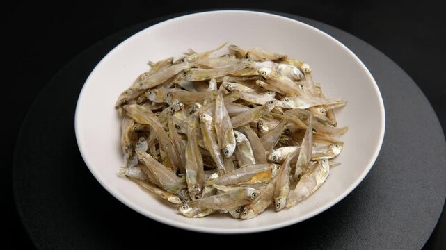 Dried Thai river sprat in white plate or Dried glass minnow (pla siu kaew).a tiny, see-through freshwater fish that is dried in the sun.