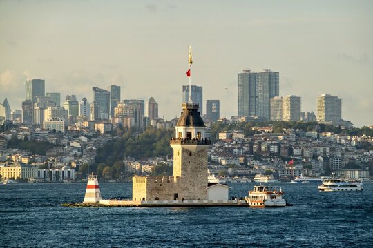 View of the historic Maiden's Tower situated on a small islet in the Bosphorus, with the modern skyline of the city in the background under soft daylight, Uskudar, Istanbul, Turkey.