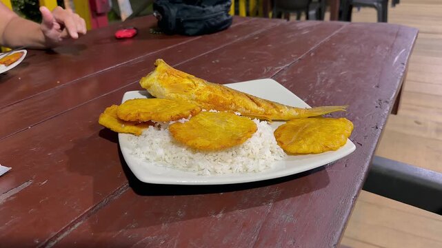 fried fish with rice and patacones on wooden table