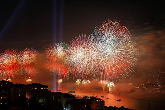 View of vibrant fireworks illuminating the night sky over the Bosphorus strait with silhouettes of boats and city buildings in Istanbul, Turkey.