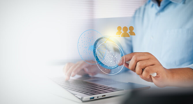 Businessman typing on laptop with digital data analysis and audience segmentation interface on white desk, Magnifying glass with data analytics, HR candidate selection, and digital marketing concept