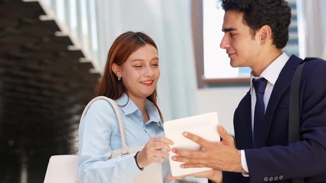 Tight two-shot of a businesswoman and a colleague going through a tablet outdoors, her question and his answer playing out in close-up against a soft and bright wall