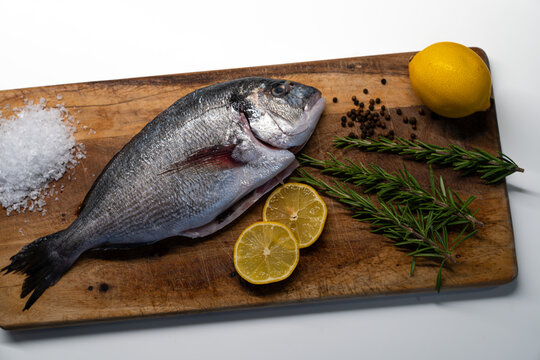 Fresh raw sea bream with lemon and rosemary on wooden cutting board
