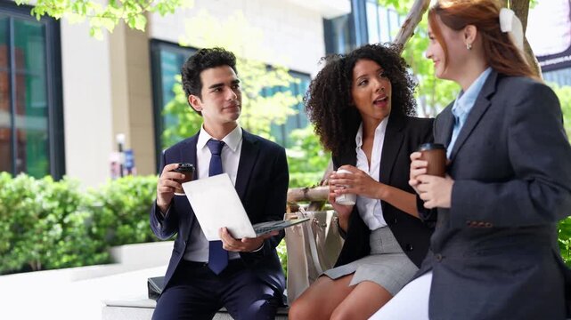 Businessman holds an open laptop while two businesswomen read over his shoulder, an impromptu team work session in the open air of a modern green city office campus