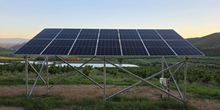 View of a solar panel array installed in a rural orchard with rolling hills in the background during golden hour in Hoeko, Western Cape, South Africa.