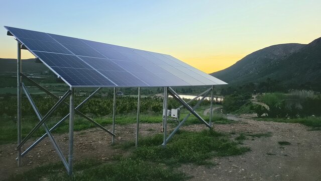 View of a solar panel array set in a rural landscape with rolling hills and a golden sunset sky in Hoeko, Western Cape, South Africa.