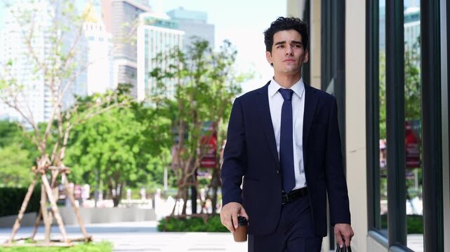 Businessman walking alone to work along a glass office facade, glancing at his watch as he keeps pace with the morning rush on a tree-lined walkway in a busy city center
