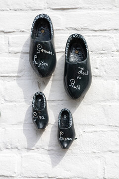 View of decorative black wooden clogs with names painted on them mounted on a white brick wall in Thorn, Limburg, Netherlands.