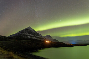 Green northern lights glowing over a mountain and lake at night © Cole