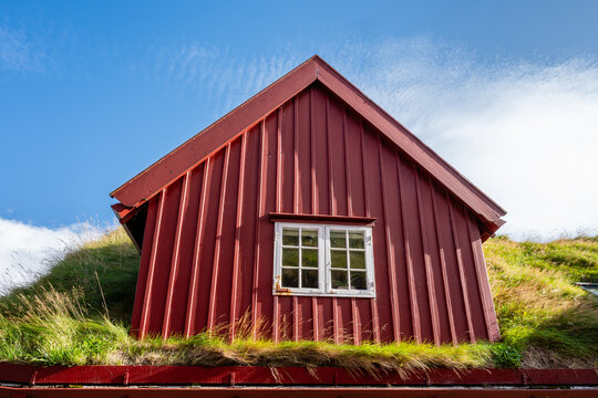 View of a traditional red wooden house with a grass roof under a clear blue sky in the Faroe Islands.