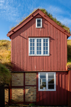 View of a traditional red wooden house with a green turf roof and brick lower level under a clear blue sky in the Faroe Islands.