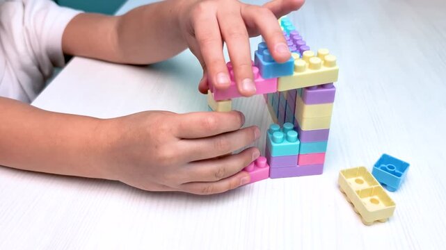 Close up video of child hands constructing a tower using colorful plastic toy building blocks. Educational game for fine motor skills development with copy space. Montessori sensorial activity