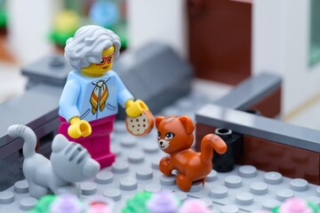 Obraz premium Tambov, Russian Federation - September 24, 2026 A Lego grandmother minifigure standing outside a house holding a miniature cookie, feeding an orange cat and a grey cat.