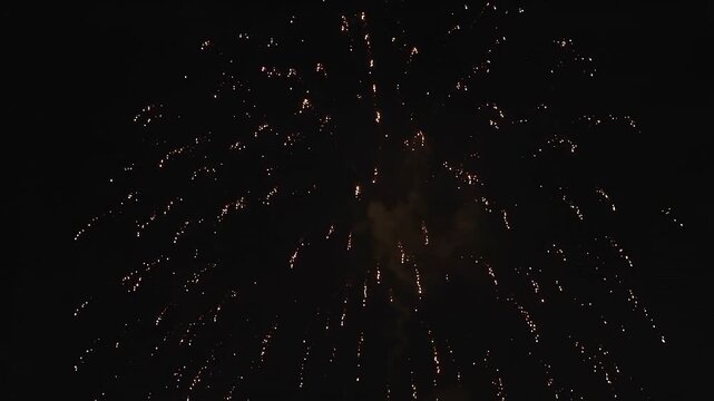 Golden fireworks exploding on dark sky during night celebration shot on black background.