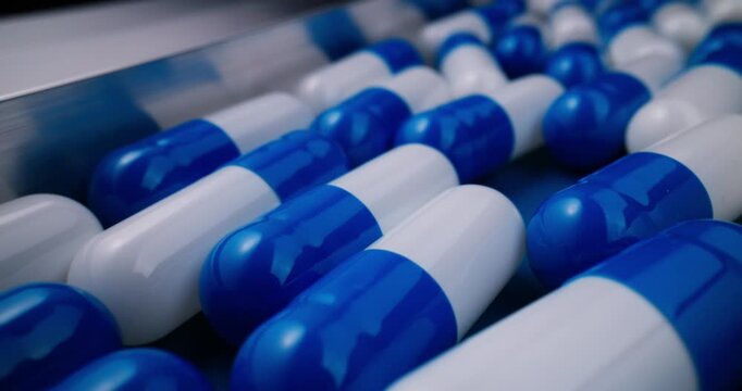 Tracking shot of blue and white capsules moving along pharmaceutical production line in factory closeup steady motion clinical sterile environment.