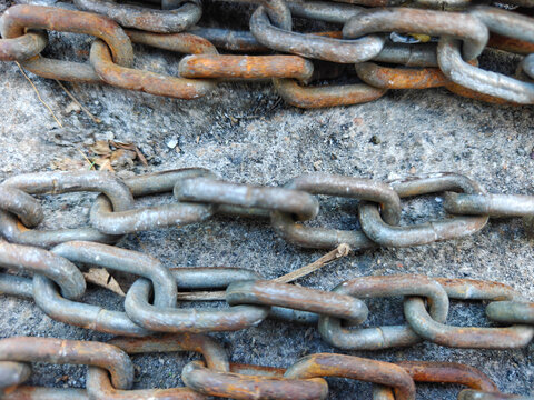 Close-up background texture of heavy metal chains with rusty links resting on concrete ground