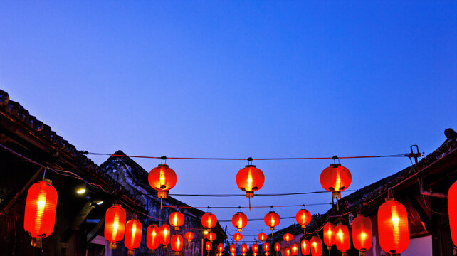 Red paper lanterns glowing over a narrow street at dusk