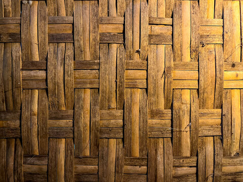 Woven bamboo strips form a tightly crisscrossed basket-weave pattern, creating a warm golden textured surface often used for traditional handmade wall and craft paneling.