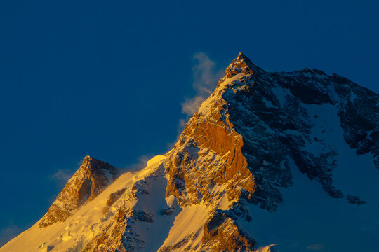 View of the snow-capped peak of Nanga Parbat illuminated by golden hour light against a deep blue sky, Fairy Meadow, Gilgit, Pakistan.