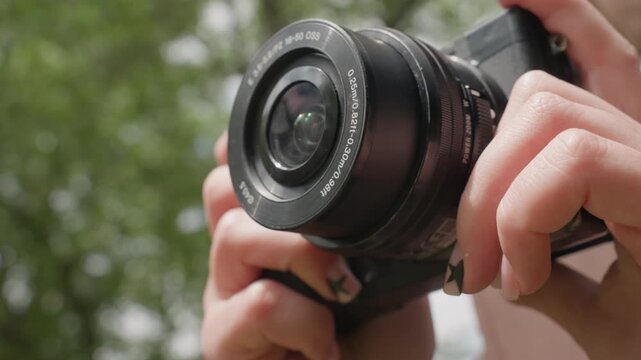 Close up shots show person hand holding and adjusting settings on digital SLR or mirrorless camera focusing lens pressing buttons. Background is consistently blurred green foliage suggesting