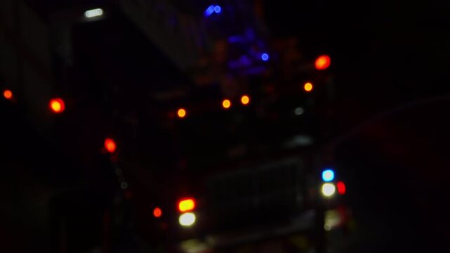 Out of focus view of fire emergency truck on accident scene at night. First responders fire vehicle rescue at city street. Fire truck with flashing emergency lights at night.