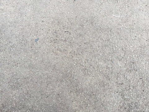 Close-up of rough gray asphalt surface with fine gravel grains and subtle speckles, creating a coarse, weathered texture suitable for urban backgrounds and construction themes.