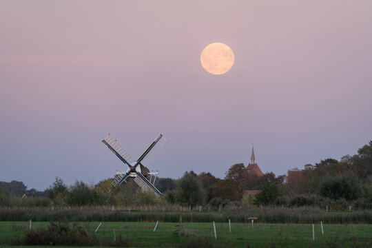 Full moon over a traditional windmill in the Dutch countryside. Groningen, the Netherlands.