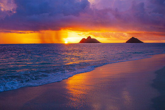 View of the vibrant sunset over Lanikai Beach with the Mokulua Islands silhouetted against a colorful sky in Kailua, Hawaii, United States.