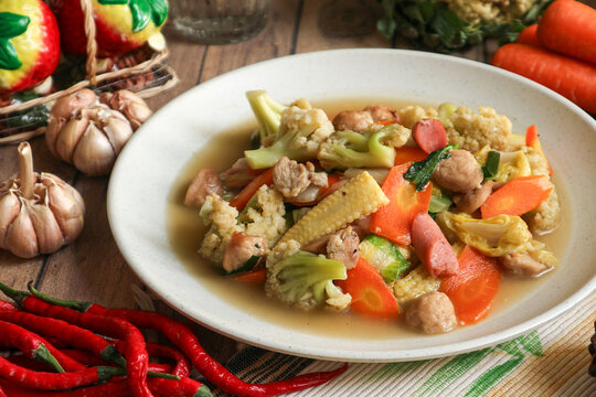 A plate of capcay, an Indonesian-Chinese stir-fried vegetable dish made with carrots, baby corn, cauliflower, chicken, and sausages in a light savory gravy.