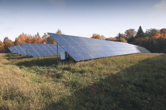 View of a solar park with rows of photovoltaic panels set in a grassy field against a backdrop of autumn trees in Otepaa, Valga County, Estonia.