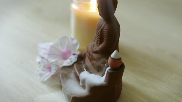 A tranquil close-up of a ceramic Buddha backflow incense burner, capturing the meditative atmosphere as smoke elegantly cascades down like a misty waterfall. 