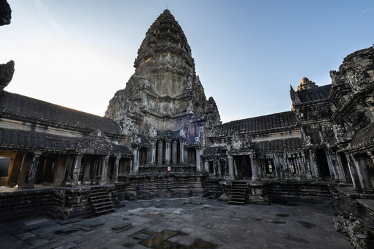 View of Angkor Wat temple complex with its iconic central tower, ancient stone carvings, and weathered sandstone walls under a clear sky in Krong Siem Reap, Siem Reap Province, Cambodia.