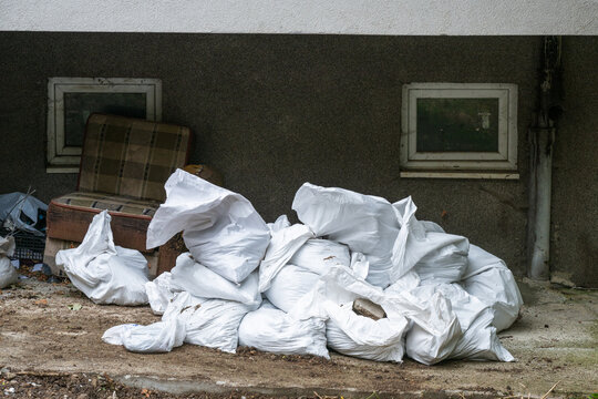 A pile of white rubble sacks and discarded furniture sit piled outside a weathered basement wall during home renovation or cleanup work.