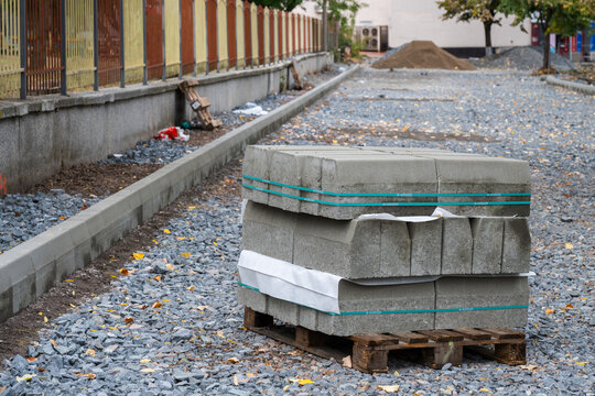 a stack of new concrete curb stones secured on a wooden pallet resting on a gravel bed at an outdoor street construction site