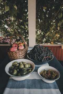 View of a basket of fresh apples, bowls of dark and light grapes, and green tomatoes arranged on a table with a striped runner in Vormsi, Laane County, Estonia.
