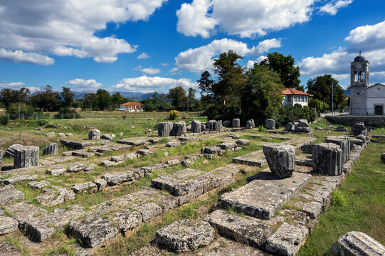 The surviving foundations and architectural blocks of the Temple of Athena Alea at Tegea, 4th century BC, with a modern church standing immediately beside the ancient sanctuary.