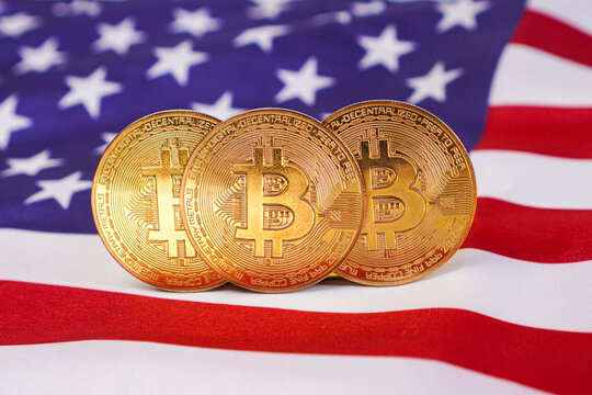Three physical gold Bitcoin tokens overlapping on the United States flag.