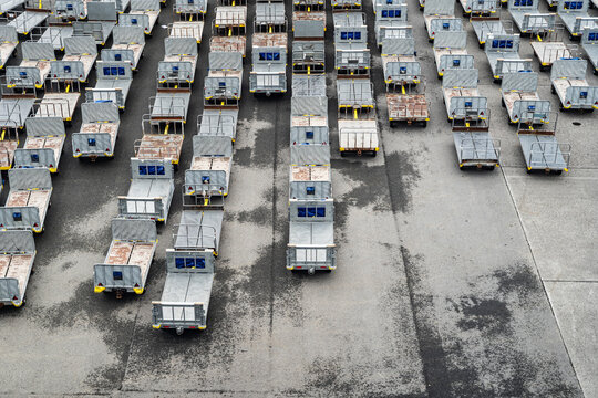 View of rows of empty airport baggage carts parked on an asphalt tarmac in Iceland.