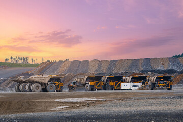 Line of large mining dump trucks parked at gold ore pit against pink sunset sky for mining industry banner © Parilov
