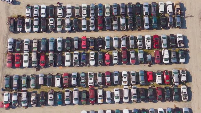 Aerial view of large car lot with rows of vehicles. Cars parked tightly in organized rows. Dirt paths separate sections of parked cars. in footage. Ideal for automotive industry, logistics