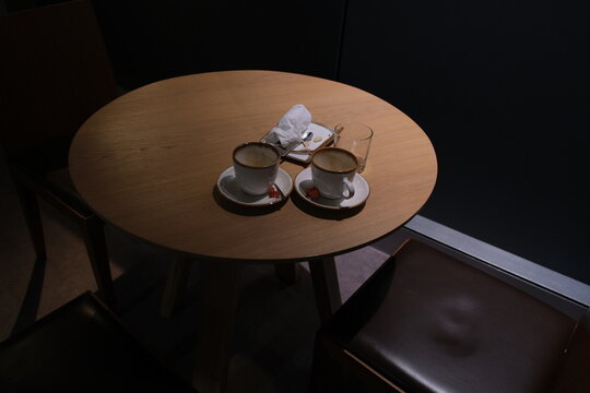 Overhead shot of two finished coffee cups with visible residue, resting on saucers next to a used napkin and an empty glass on a round wooden table.