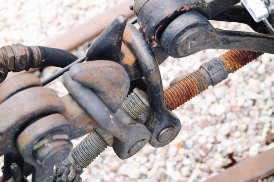 Rusty railway mechanical linkage with threaded rods and heavy steel joints. Weathered industrial hardware close detail. Railroad engineering background. Corroded metal components and bolts.