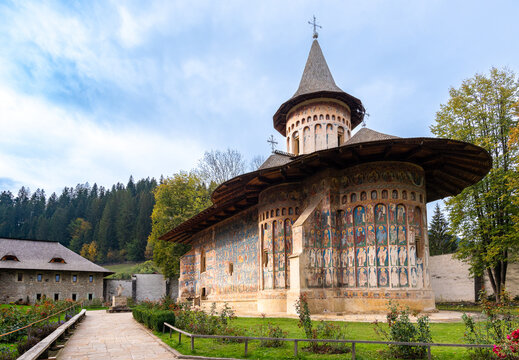 View of Voronet Monastery with its iconic exterior frescoes, stone walls, and surrounding trees in Voronet, Judetul Suceava, Romania.
